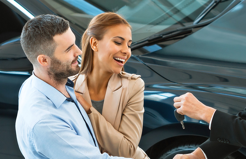 A smiling young couple are being given the keys to a new GMC SUV in the showroom
