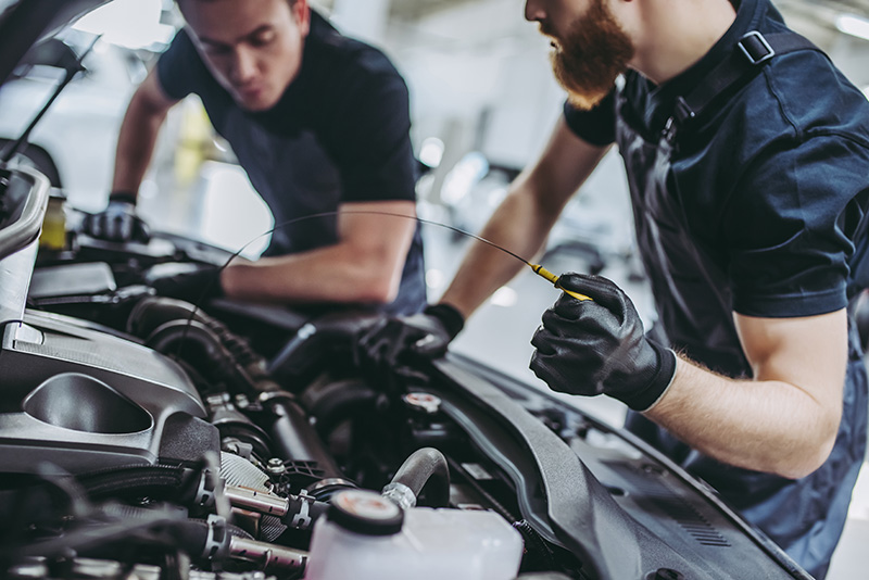 2 certified maintenance professionals in black outfits and gloves service a GMC SUV engine.